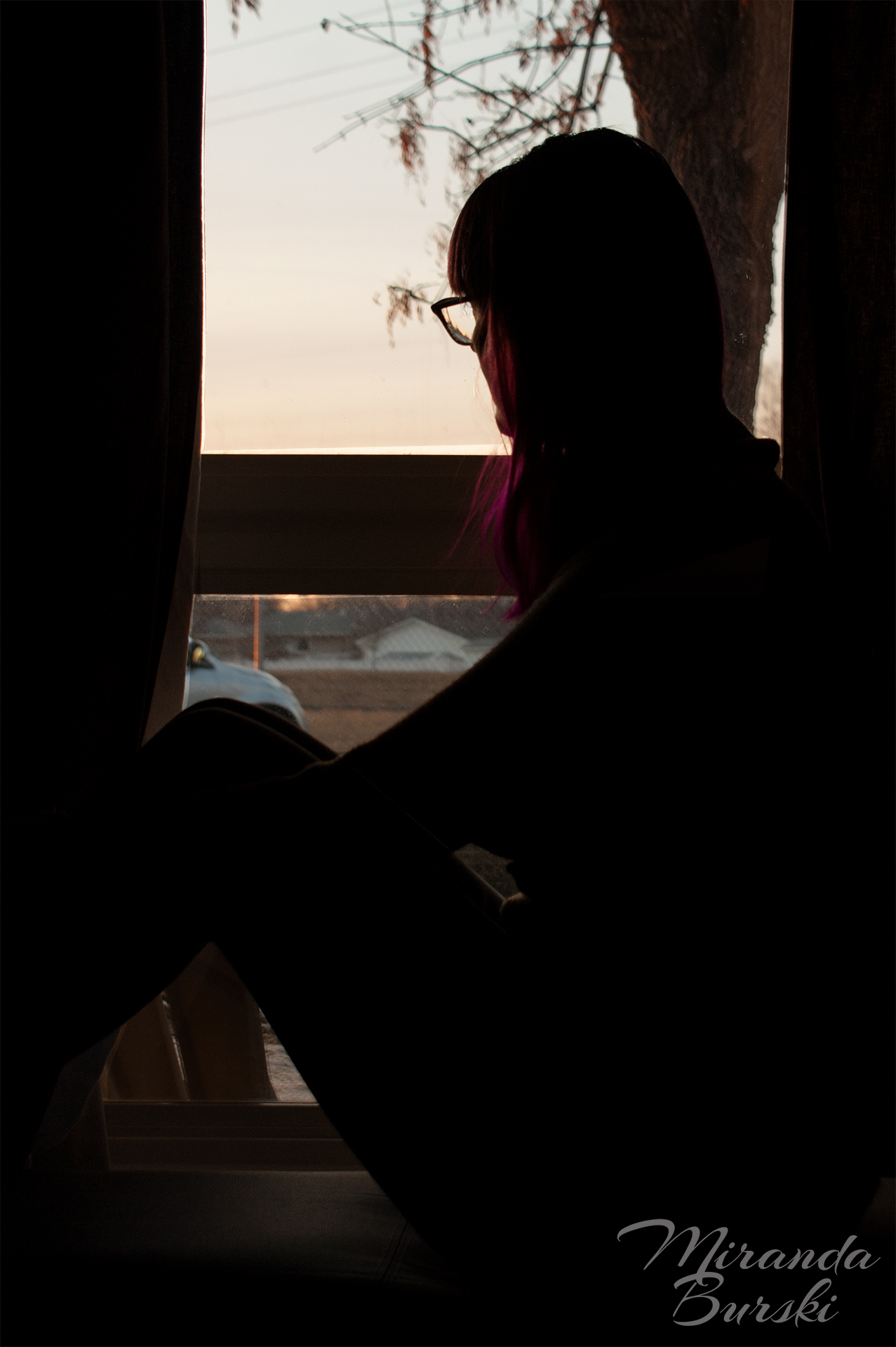 A woman sitting in a window, silhouetted by a sunset.